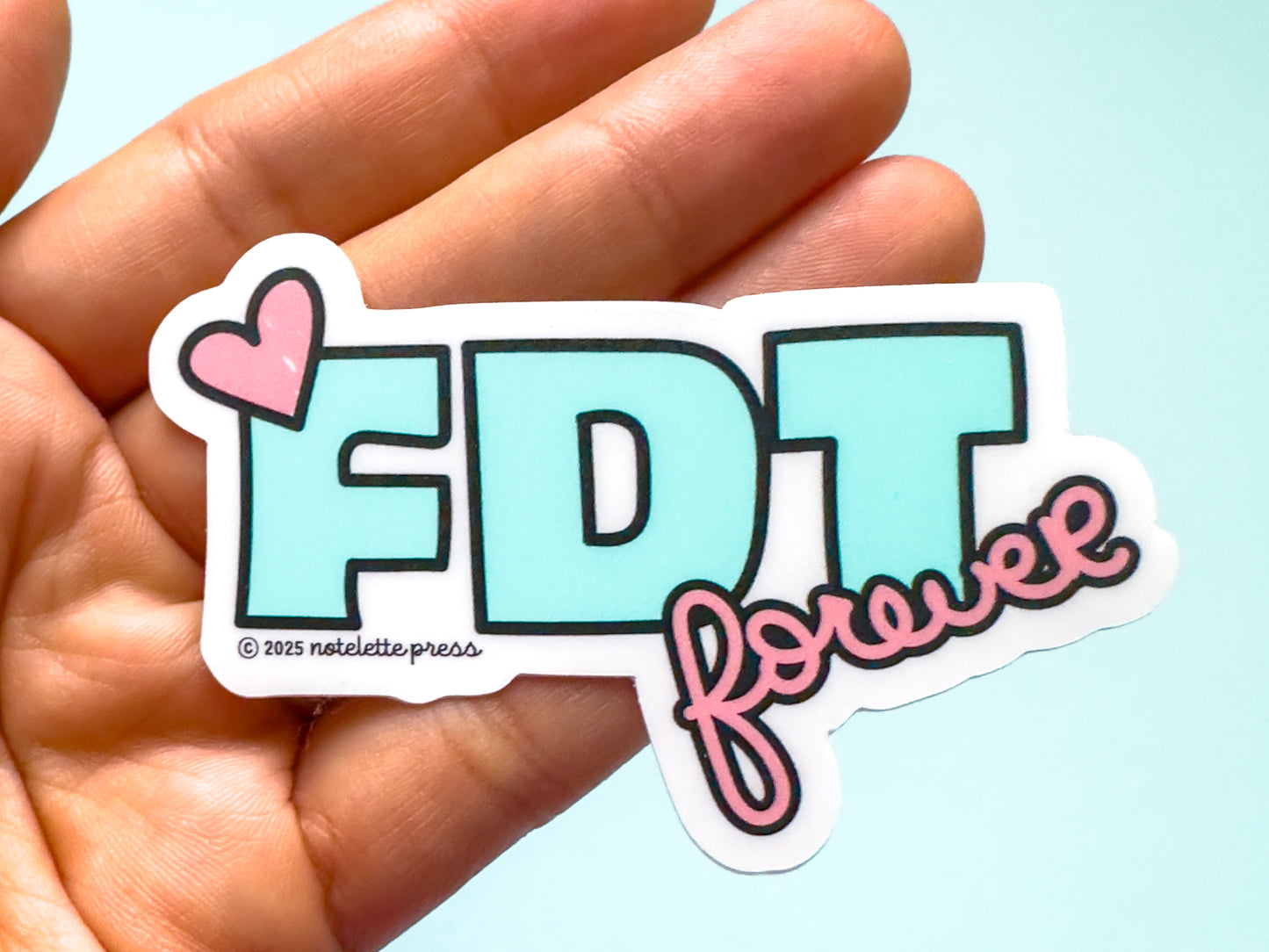 Sticker with 'FDT forever' text held in a hand against a light blue background