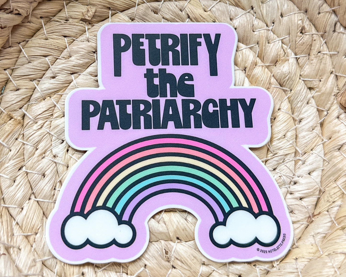 Sticker with rainbow and text 'PETRIFY THE PATRIARCHY' on a woven background