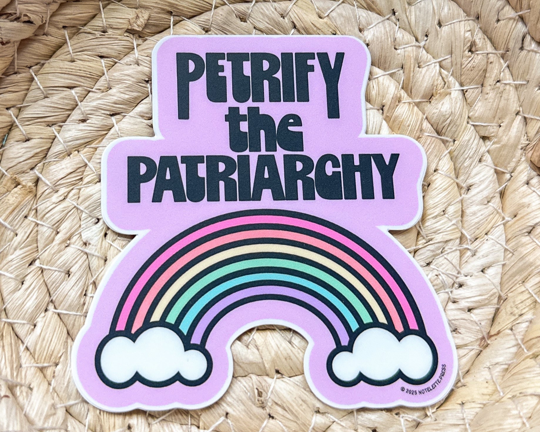 Sticker with rainbow and text 'PETRIFY THE PATRIARCHY' on a woven background